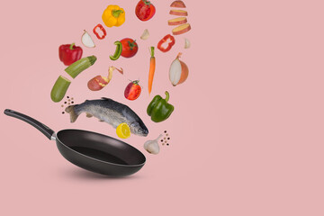 Raw trout fish with different vegetables and lemon flying above frying pan for tasty cooking, isolated on bright pink background.