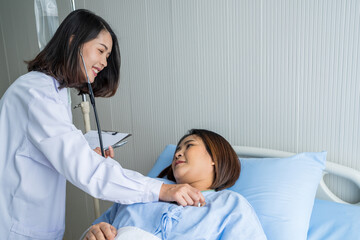 Fototapeta premium Female doctor checking the health of an Asian female patient lying on the bed. At the hospital, the doctor and patient are smiling.
