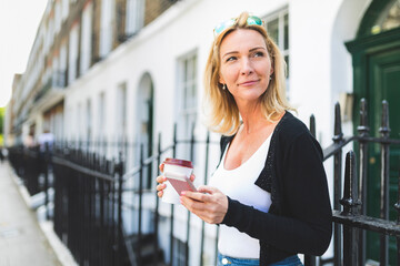 Smiling mature woman looking away while holding coffee cup and smart phone