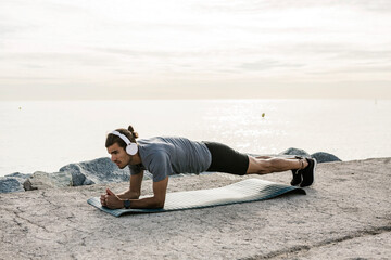 Male athlete with headphones exercising plank position on exercise mat