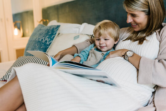 Cute boy watching photo album with pregnant mother in bedroom