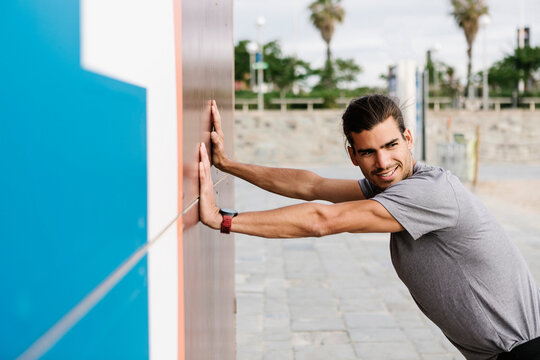 Smiling Male Athlete Exercising While Leaning On Wall