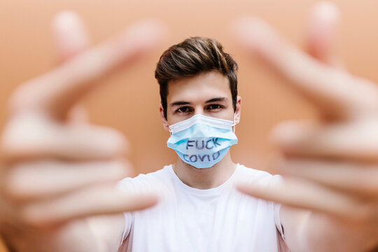Man wearing protective face mask with text gesturing in front of wall