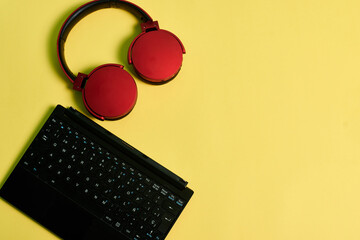 Computer keyboard and red headphones on a yellow background