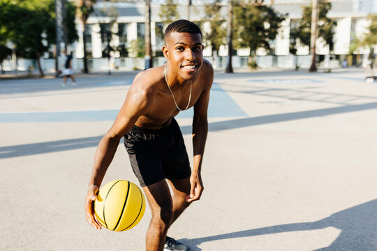 Shirtless young man practicing basketball at sports court