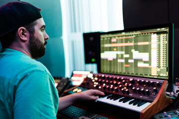 Mid adult male artist playing synthesizer while mixing sound in studio
