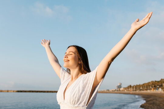 Smiling woman with arms outstretched standing at beach