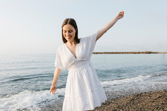 Carefree young woman with arms outstretched walking at beach
