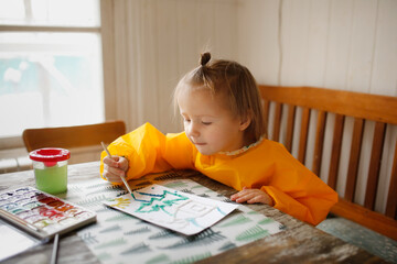 cute caucasian child Toddler is engaged in creativity in a yellow protective apron, the child draws with paints on salt, unusual drawing and developmental activities