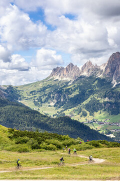 A group of unrecognizable young mountain bikers ride downhill in the Italian Dolomites (Vertical photo)