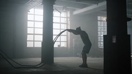 Fototapeta na wymiar Guy battling ropes during training session. Sportsman performing intense workout