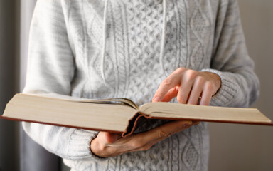 Close-up of a man reading into a huge old book. Selective focus on the index finger.