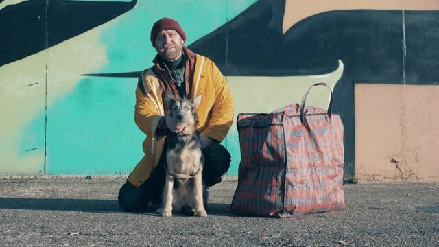 A poor man is petting his dog in the city street