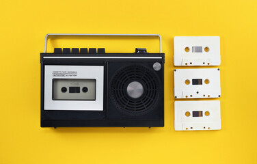 Fototapeta premium Antiquated retro-style portable stereo radio with cassette recorder and audio cassettes from around the late 70s on a yellow background. Music listening concept. Vintage. 