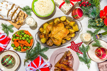 Festive Christmas dinner table with traditional foods and dished – baked ham, chicken, roasted carrots and brussels sprouts, potato, with Christmas decor and gifts 