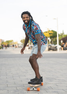 Positive black man riding longboard on street