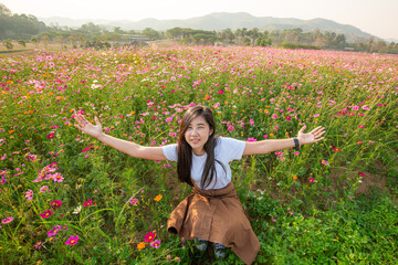 Asian girl in white dress sits in a meadow of pink flowers in the countryside in summer with copy space for graphic design.