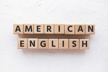Text AMERICAN ENGLISH on wooden cubes on white putty background. Learning languages. Flat lat, top view.