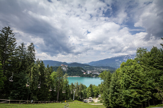 Panorama of the Bled lake, Blejsko Jezero, with its castle, Blejski Hrad, with the mountains of Julian alps in front of stopped ski lifts, not working in summer, in ski resort of straza bled, slovenia
