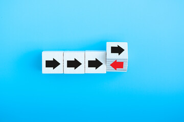 Red arrow flip over wooden cube block with red arrow opposite directon black arrows think different and standing out from the crowd concept isolated on blue background.