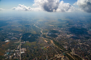 Aerial view from airplane window at high altitude of distant city covered with white puffy cumulus clouds