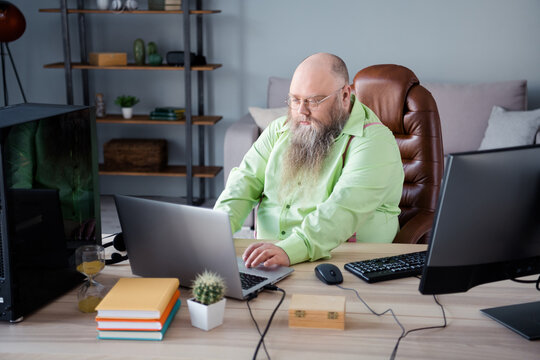 Photo of serious overweight bearded bald programmer guy sit desk work laptop coding home office workstation