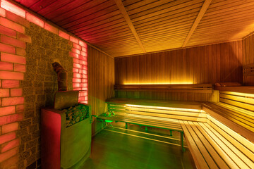 sauna interior with a large brick wall and natural wood trim, stove with stones to humidify air and steam, atmospheric lighting