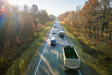 Aerial view of intercity road with fast driving cars between autumn forest trees at sunset. Top view from drone of highway traffic in evening