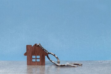 Wooden house and keys on a metal chain against a gray wall. New home buying concept