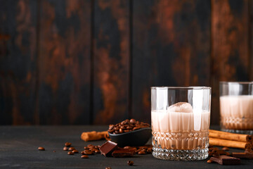 Glass of Irish cream baileys liqueur with roasted coffee beans, cinnamon and chocolate on dark wood...