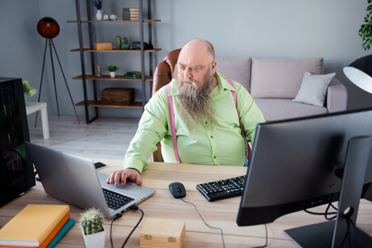 Photo of focused concentrated young man look laptop work sit desk coder indoors inside house office workstation