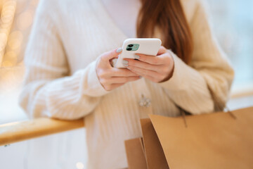 Close-up cropped shot of unrecognizable young woman using typing smartphone holding shopping bags...