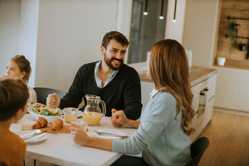 Young happy family talking while having breakfast at dining table