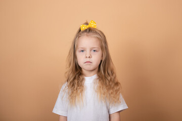 portrait of a sweet blonde little girl in white t-shirt and with yellow bow on her head. on brown background.