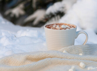 white cup with cocoa and marshmallows on the snow