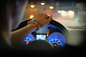 Close up of driver hands holding steering wheel driving car with blurred city street lights on...