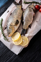 Fresh raw whole fish of mirror carp with spices, lemon and herbs on a background of parchment paper, lies on a wooden black background of boards