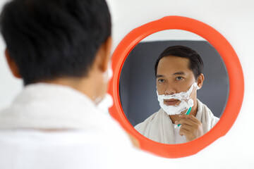 Mature handsome Asian man shaving in front of mirror