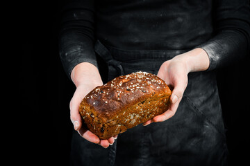 Bran bread with dried fruits in women's hands. Black baking background.