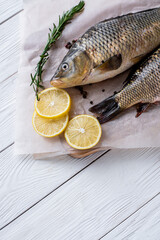 Fresh raw whole fish of mirror carp with spices, lemon and herbs on a background of parchment paper, lying on a wooden white background of boards