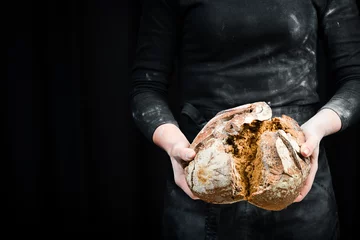 Fotobehang Bakkerij Hands break black bread from flour. Black cooking background. Isolated on black background.