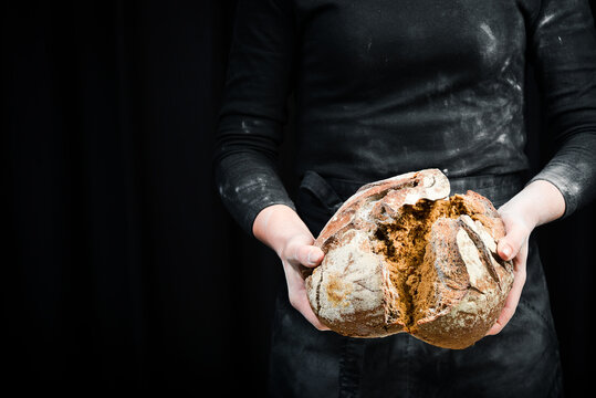 Hands break black bread from flour. Black cooking background. Isolated on black background.