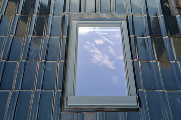 Closeup of attic window on house roof top covered with ceramic shingles. Tiled covering of building