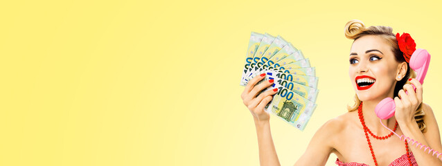 Happy smiling woman with money cash, talking on phone, dressed in pin up style, on light yellow background. Blond girl in retro fashion and vintage concept. Wide composition with copy space area.