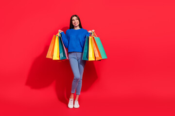 Full size photo of dreamy young charming woman look empty space hold bags isolated on red color background