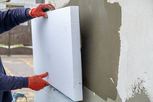Construction worker installing styrofoam insulation sheets on house facade wall for thermal protection