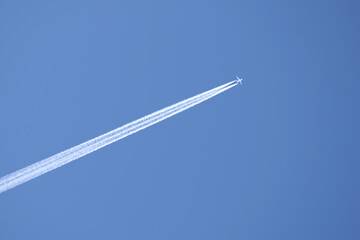 Distant passenger jet plane flying on high altitude on clear blue sky leaving white smoke trace of contrail behind. Air transportation concept