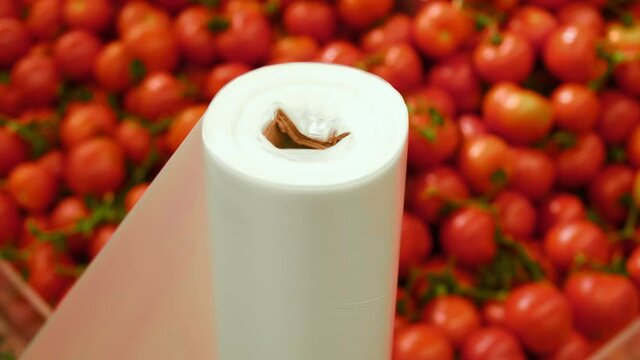  buyer tear off a plastic bag in a supermarket against the background of a vegetable shop with fresh tomatos. High quality 4k footage