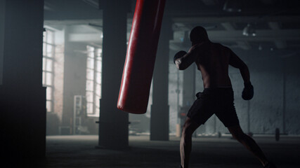 Sportsman doing intensity training. Man kicking punch bag during boxing workout