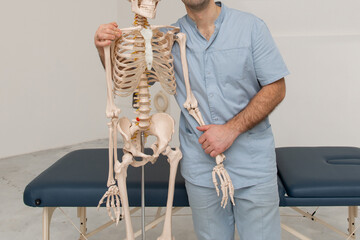 Doctor man pointing on arm of human skeleton anatomical model. Physiotherapist explaining joints...